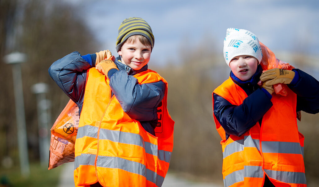 zwei Kinder in Warnwesten tragen Müllsäcke der Frühjahrsputz-Aktion